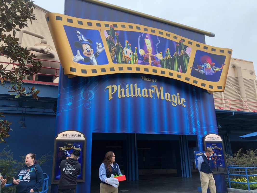 Entrance to Mickey’s PhilharMagic Opens in California Adventure, with staff and guests outside, and a blue sign on filmstrip.