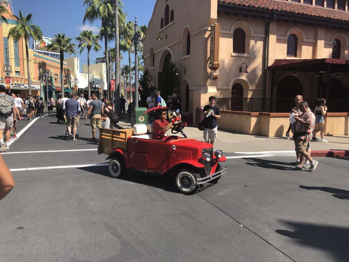 A Citizen of Hollywood drives a tiny red car through the streets