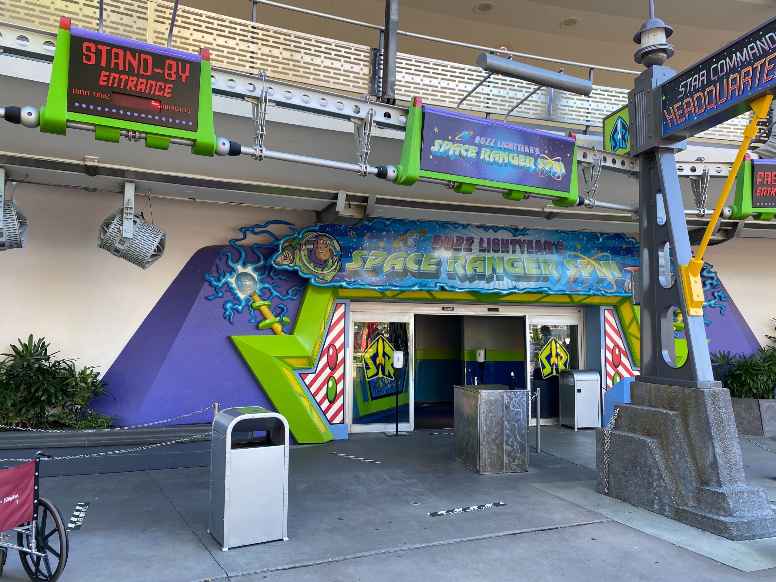 The entrance to Buzz Lightyear's Space Ranger Spin attraction bursts with colorful signs and themed decor, featuring a standby entrance and barricades at the front.