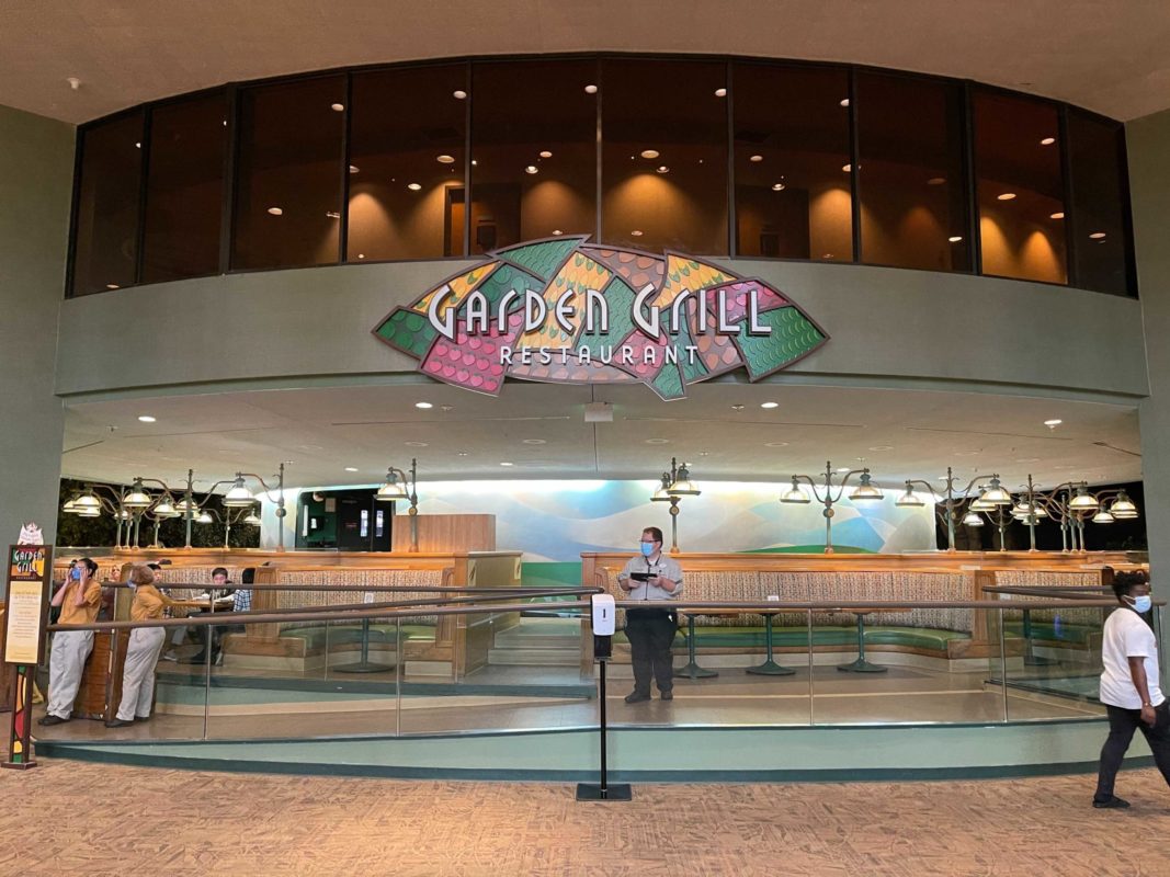 Front view of Garden Grill Restaurant entrance with a large, colorful sign and a staff member standing in front, while a few guests wait near the entrance.