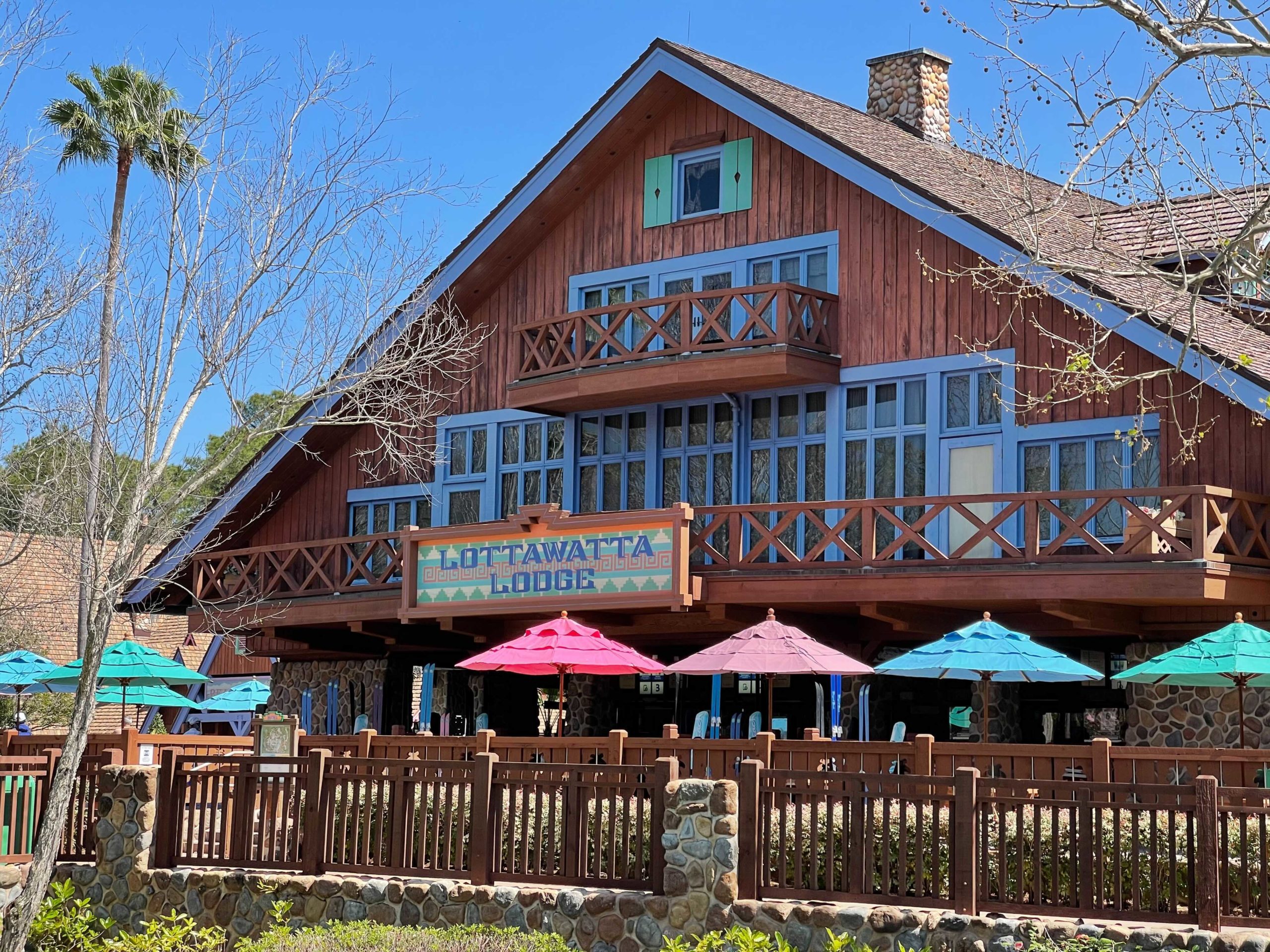 Nestled under a clear blue sky, Lottawatta Lodge stands with its charming wooden facade. Colorful umbrellas adorn the patio, creating a picturesque spot. Experience this warm haven yourself—it's worth every bit of praise in any Lottawatta Lodge review.