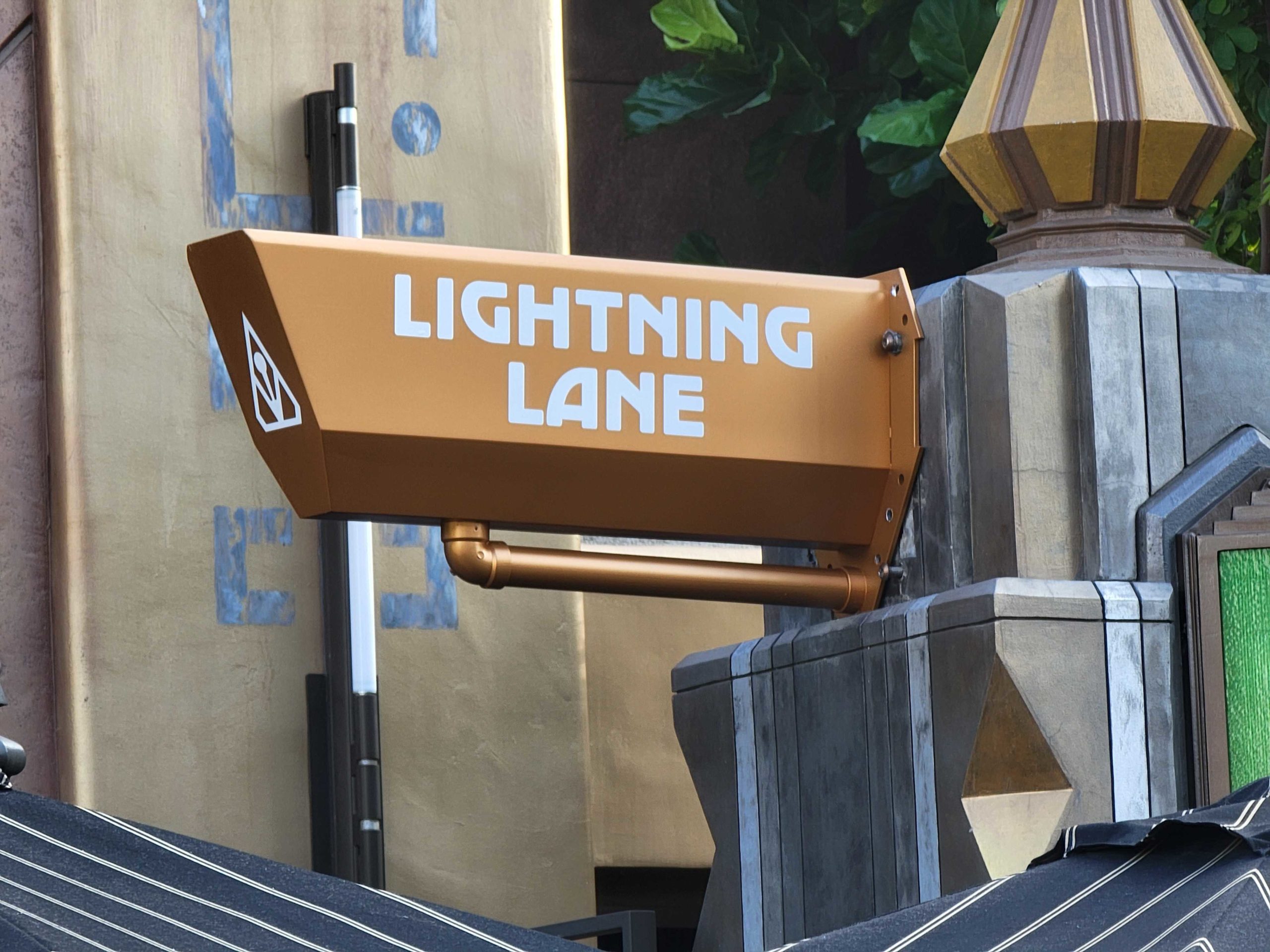 Sign with bold white lettering reads "LIGHTNING LANE" on a gold background, capturing the enchanting spirit of Disneyland as it adorns an ornate pillar.