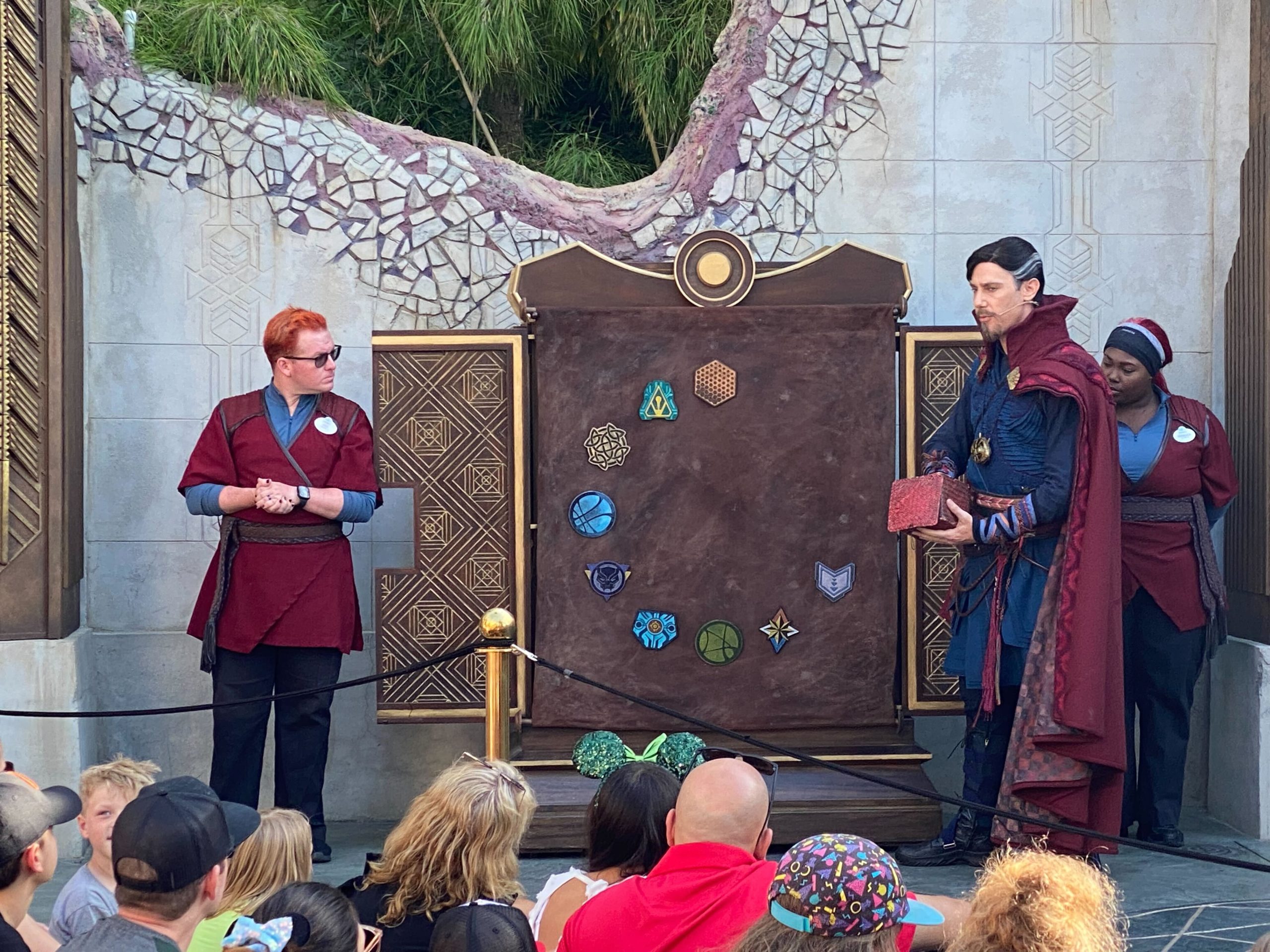 Dr. Strange in Ancient Sanctum in front of a board of colorful circular medallions, with a Cast Member in a red uniform