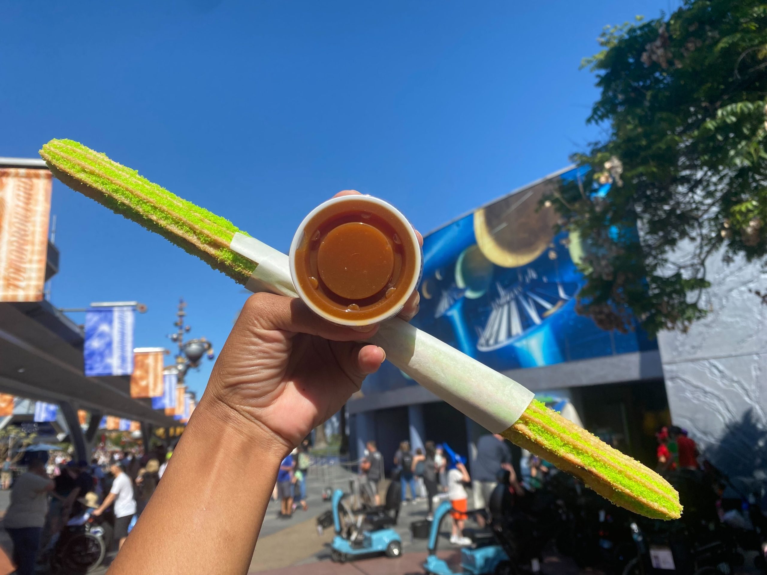 Green churro held up with a container of caramel sauce