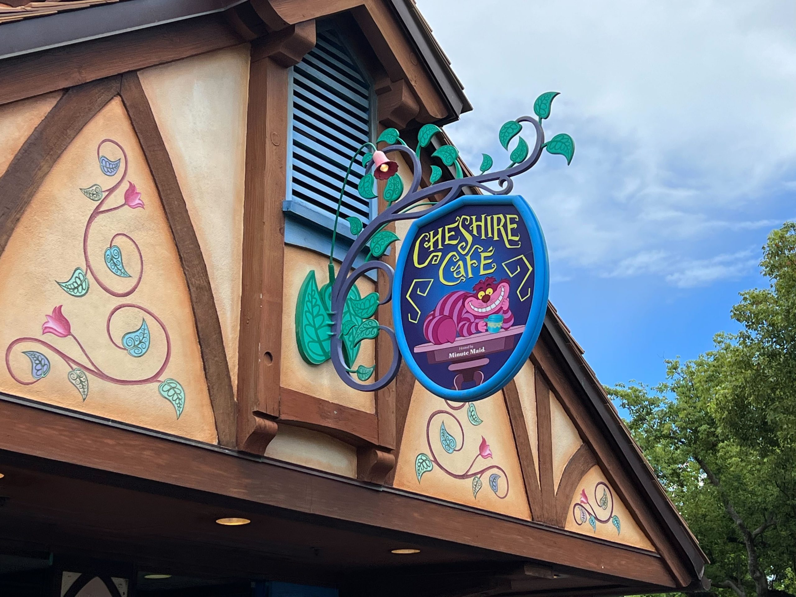 Cheshire Cafe sign featuring Cheshire Cat hanging from vine on medieval-style building facade