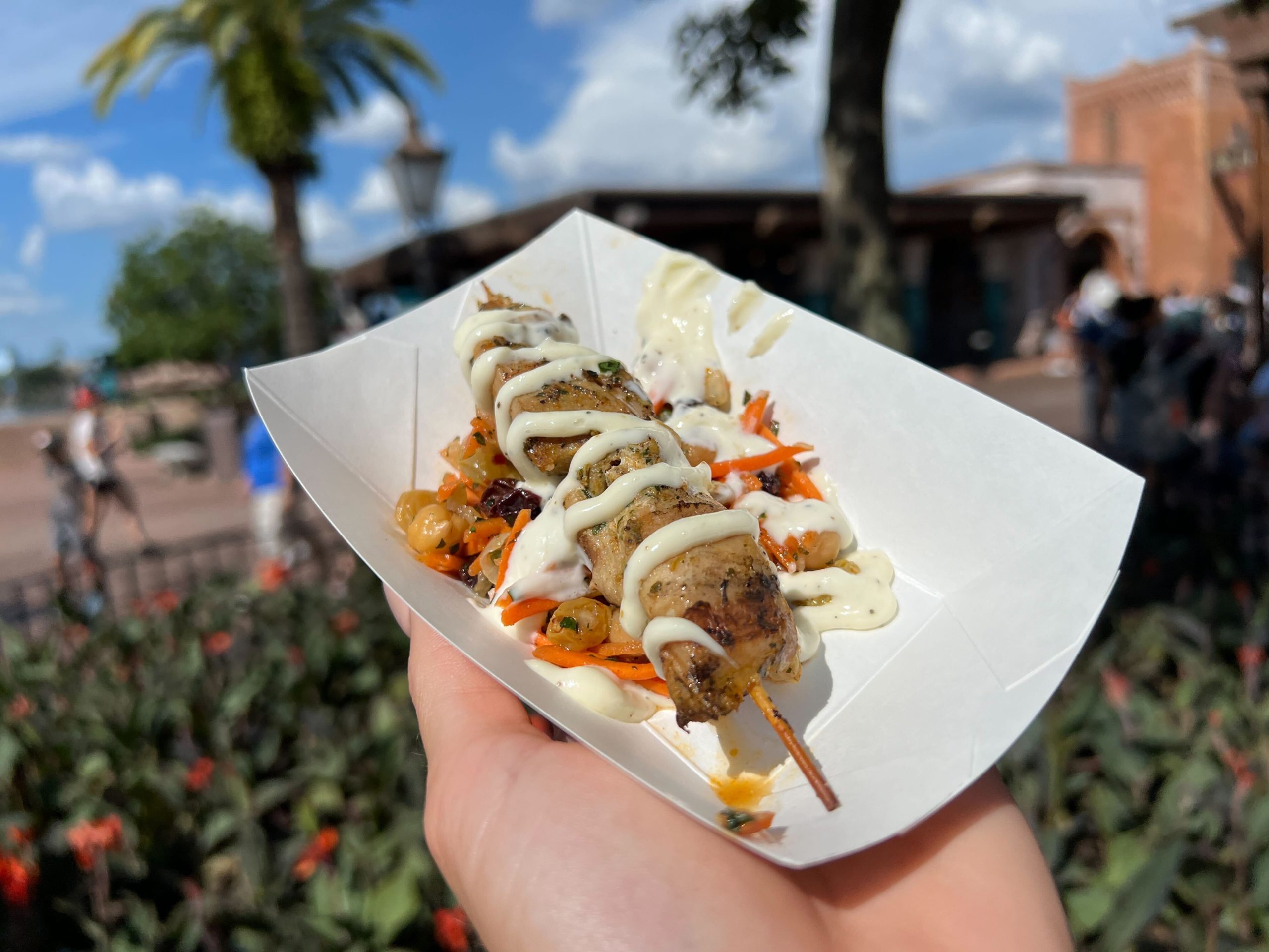 A small paper boat bowl with a chicken kebab, drizzled with white aioli.