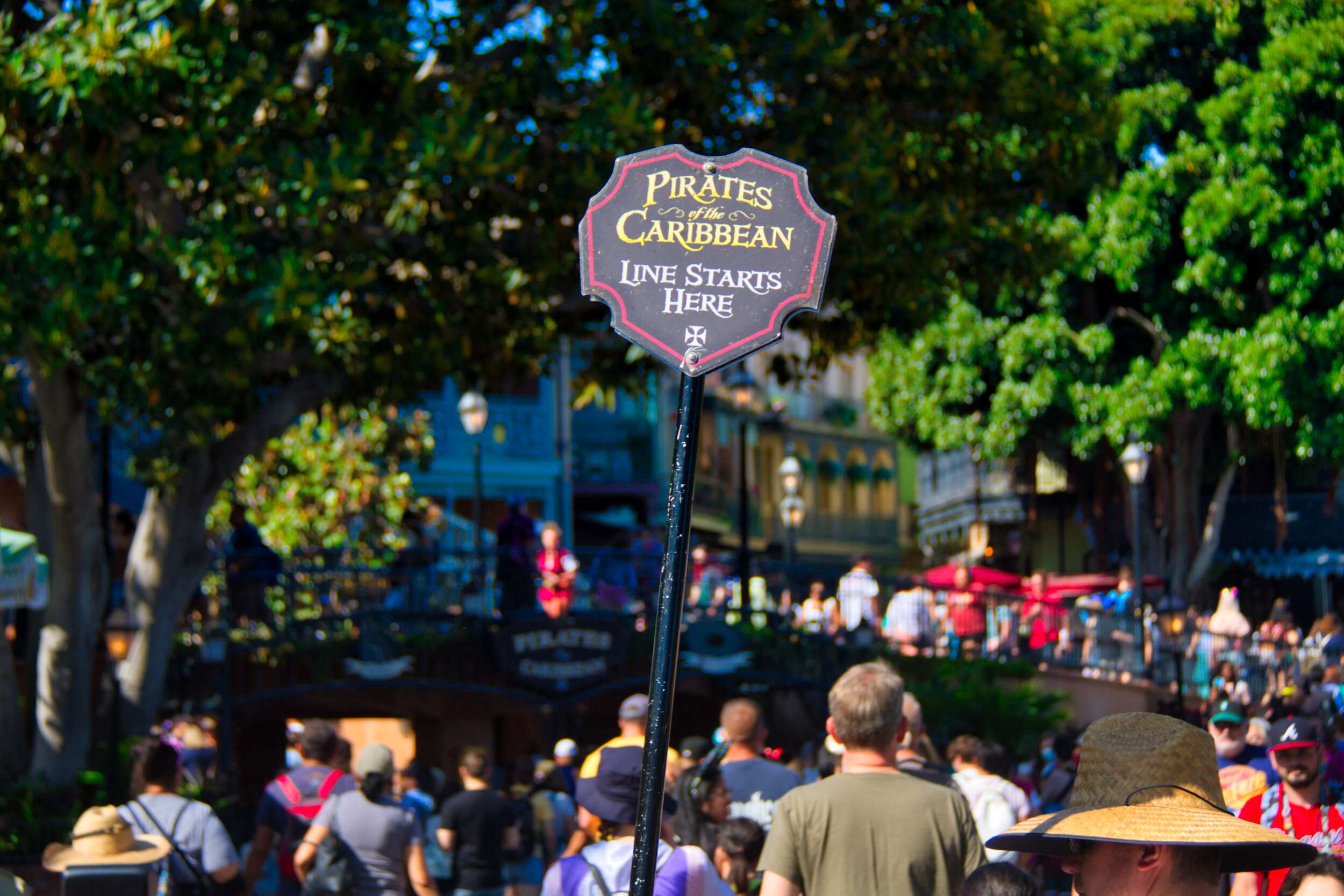 "Pirates of the Caribbean Line Starts Here" sign on a pole above crowd of people