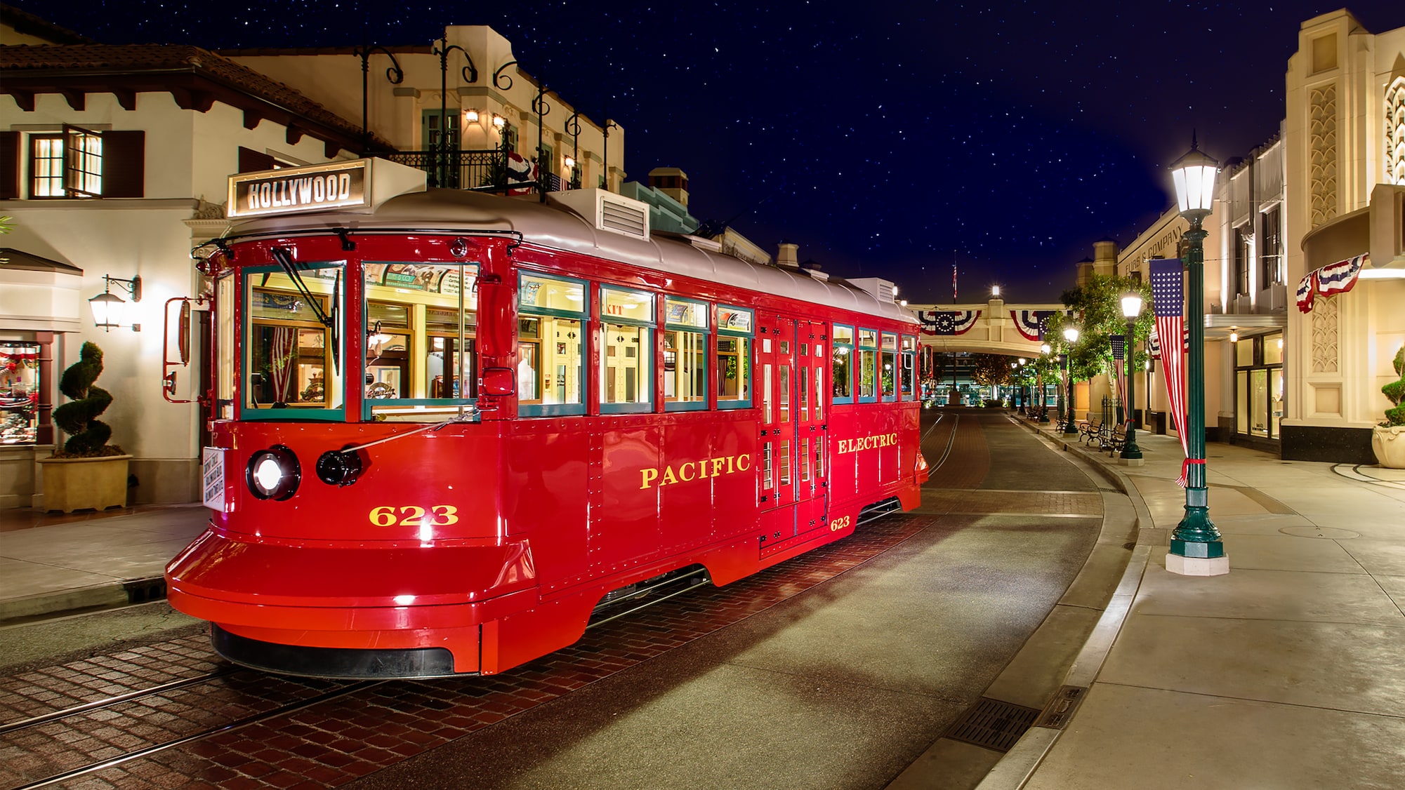 A red vintage streetcar labeled "Pacific Electric" is halted on a lit street at night, under a starry sky with buildings flanking either side—a scene reminiscent of those captured in the WDWNT Daily Recap 7.15.22.