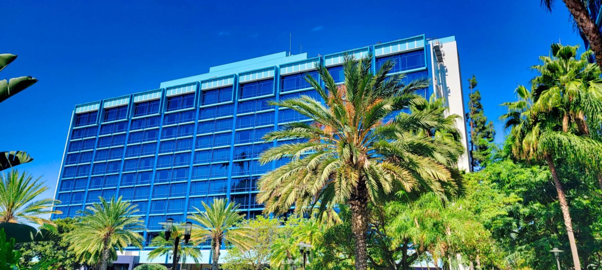 A modern blue glass building surrounded by palm trees under a clear blue sky.