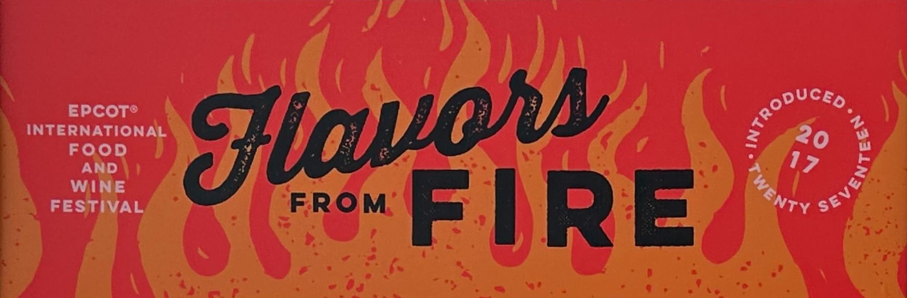 A "Flavors from Fire" sign adorned with flame graphics, part of the EPCOT International Food and Wine Festival, launched in 2017.