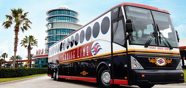 On embarkation day, a Disney Cruise Line bus is parked in front of a modern building, surrounded by swaying palm trees.