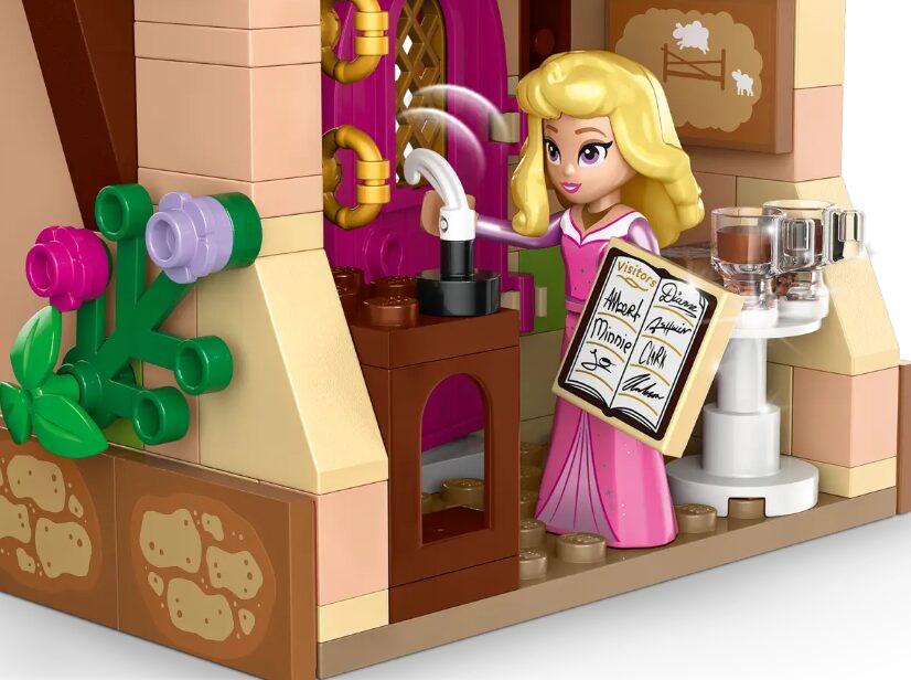 A LEGO mini doll of Princess Aurora creates delicious beverages. She holds a guest book signed by various Disney friends.