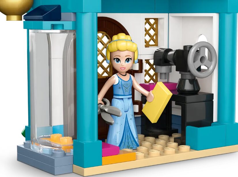 A LEGO mini doll of Cinderella holds a pair of scissors and a LEGO rectangle of fabric. She stands beside a black LEGO sewing machine.