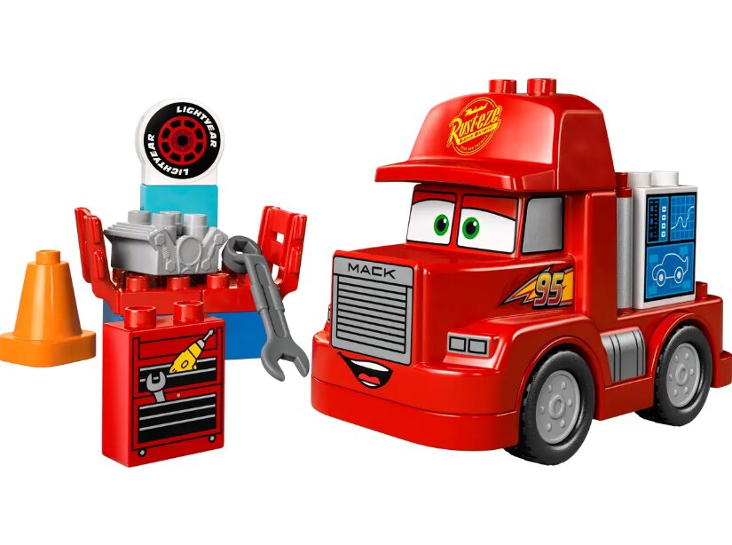 All of the included pieces in the LEGO Duplo Mack at the Race set, including a traffic cone, Lightyear tire, wrench, engine, toolbox, and Mack the truck.