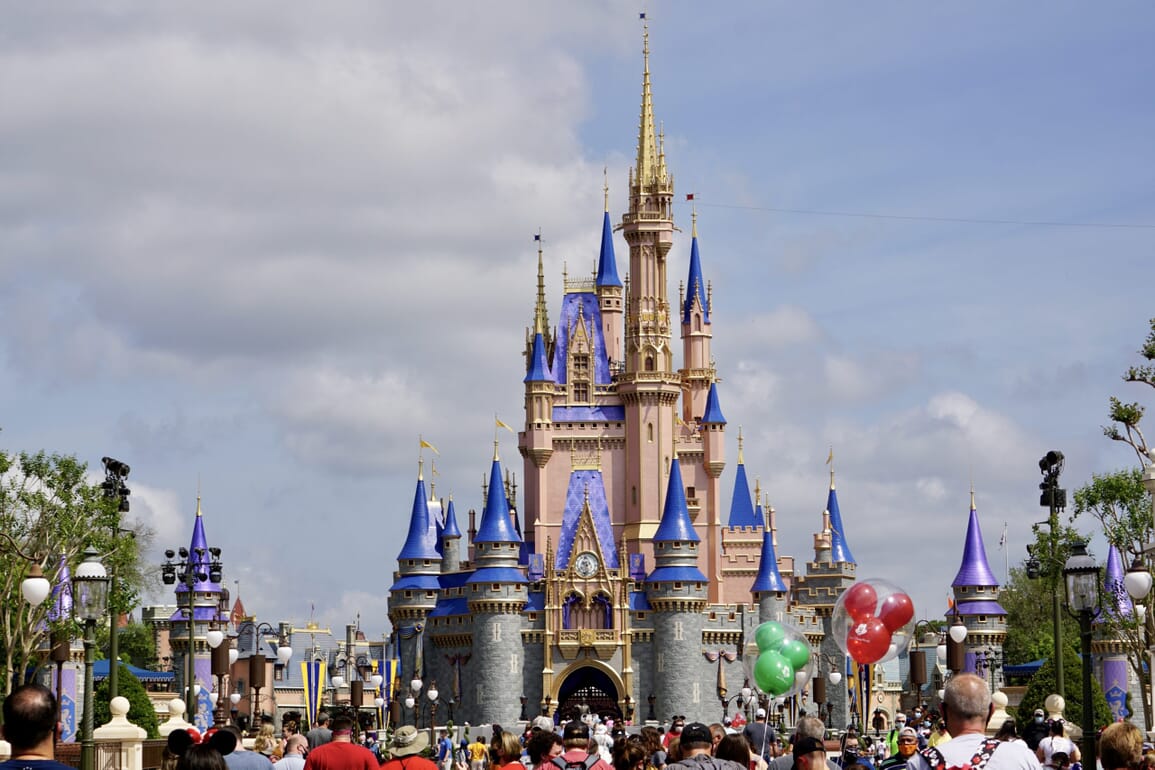 Cinderella Castle at Magic Kingdom. A crowd of guests is in front of the castle, some holding Mickey balloons.