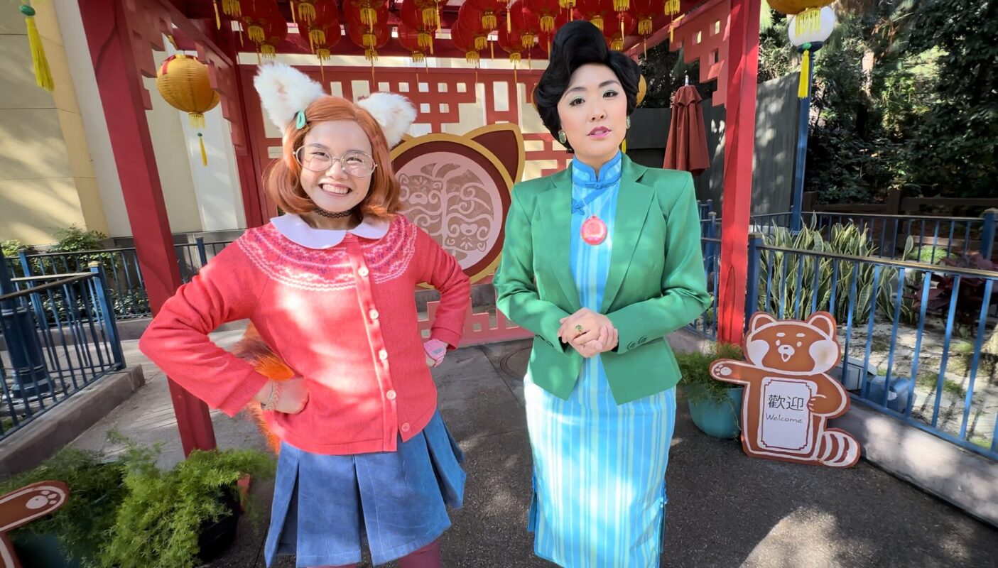 Meilin, with red panda ears and tail, smiling next to her stern mother, Ming Lee, in front of a red Lunar New Year set.