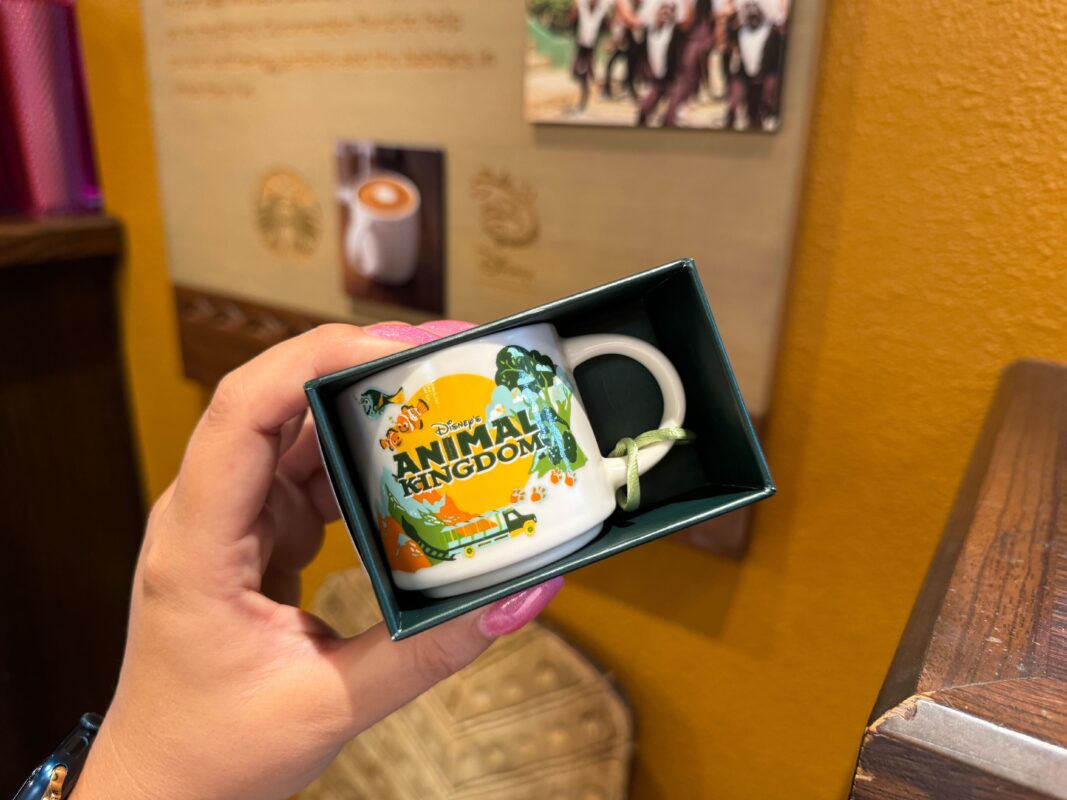 A reporter holds up the Disney's Animal Kingdom Starbucks espresso mug ornament in its box.