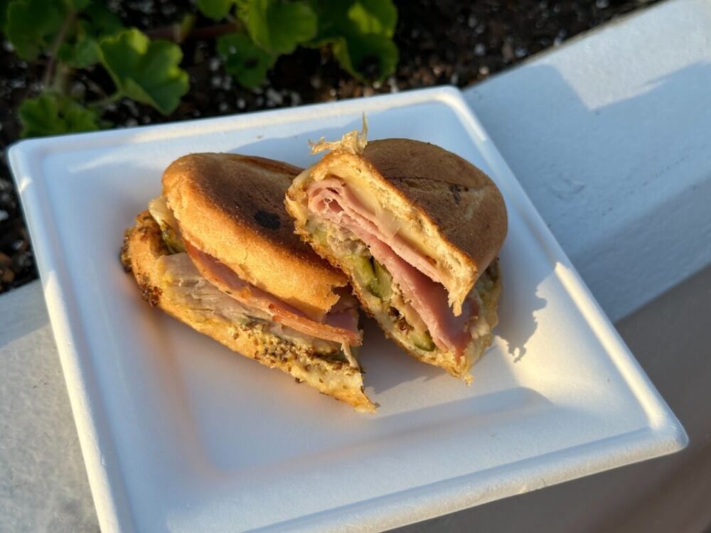 A white square plate with two halves of a Cubanito sandwich.