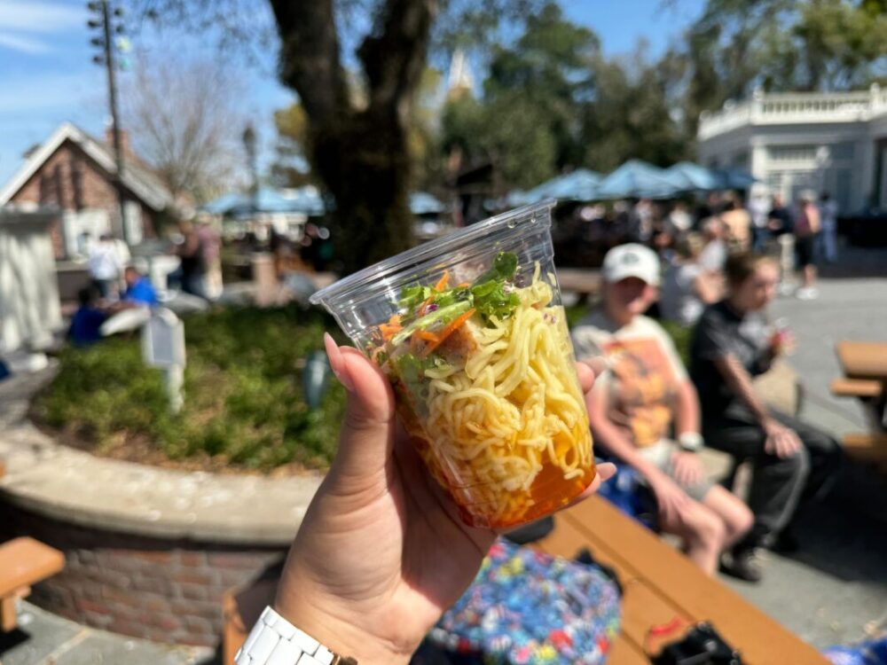 A clear plastic cup filled with ramen noodles and toppings.