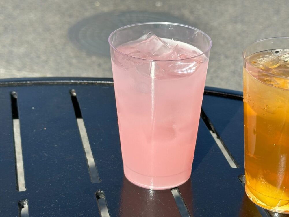 A clear plastic cup with a light pink cocktail.