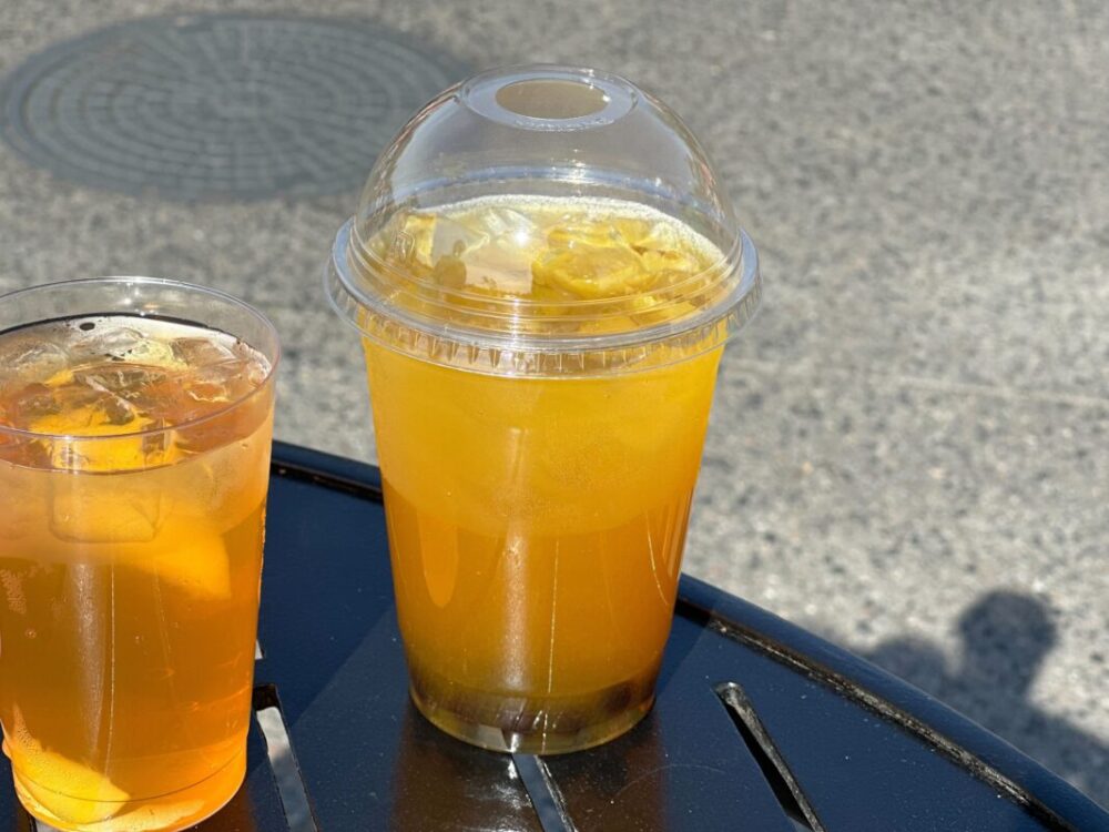 A plastic cup with a yellow drink and dark boba at the bottom.