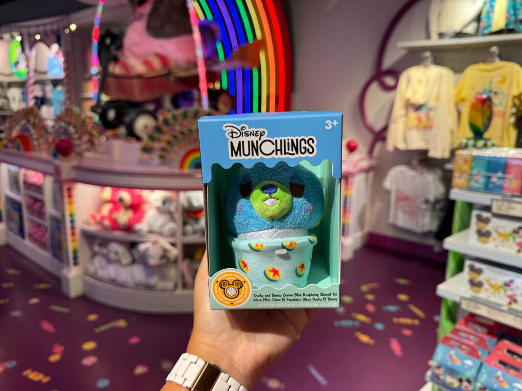 Hand holding a Disney Munchlings toy box featuring Bunny from "Toy Story 4," in a colorful store during Pixar Fest with merchandise in the background.