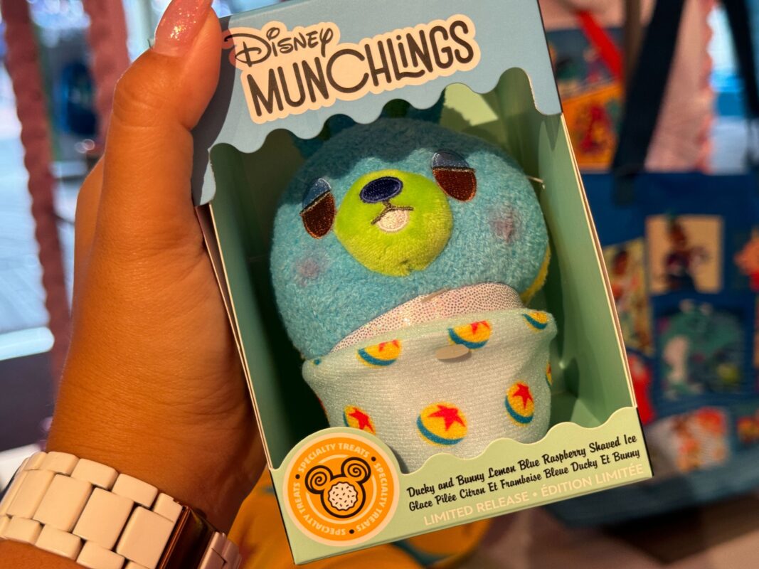 Hand holding a Pixar Fest Disney Munchlings plush toy packaged in a box, resembling a lemon blue raspberry shaved ice dessert, marked as a limited edition.