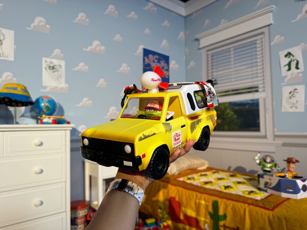 A reporter's hand holding the Pixar Fest Pizza Planet Truck popcorn bucket.