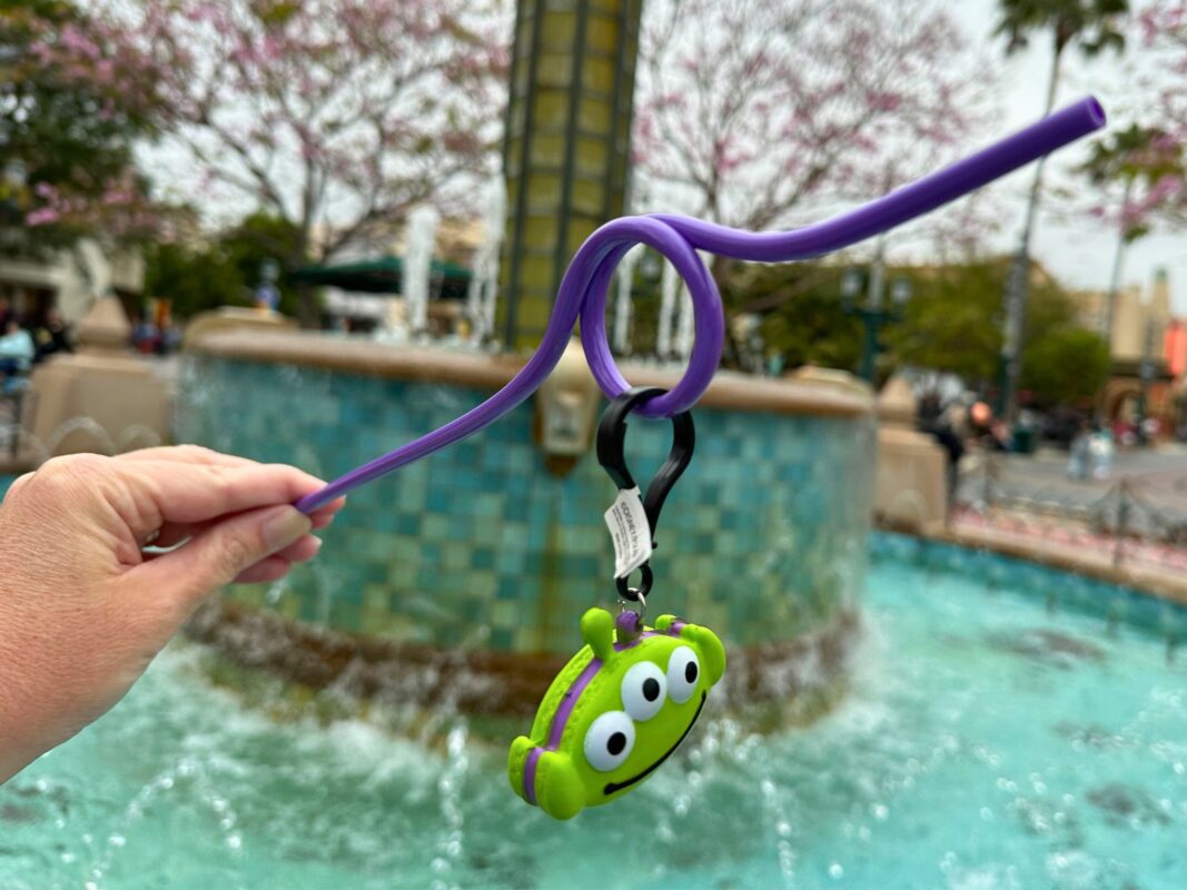 A reporter's hand holding a purple straw at an angle with the Alien Macaron Straw Clip dangling.