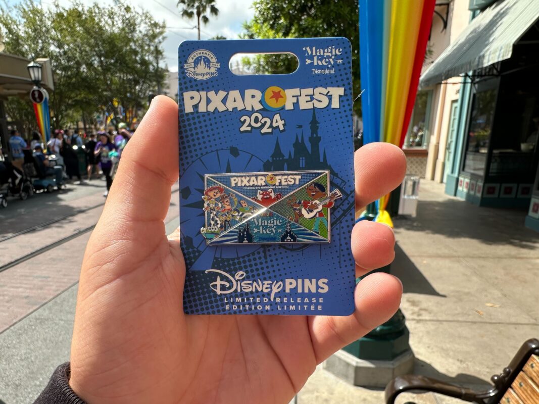 A reporter's hand holding a Magic Key Pixar Fest pin.