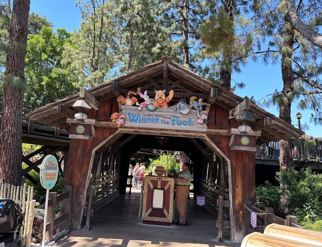 Entrance of the "winnie the pooh" ride at Disneyland, featuring wooden structure with character plushies above the sign.