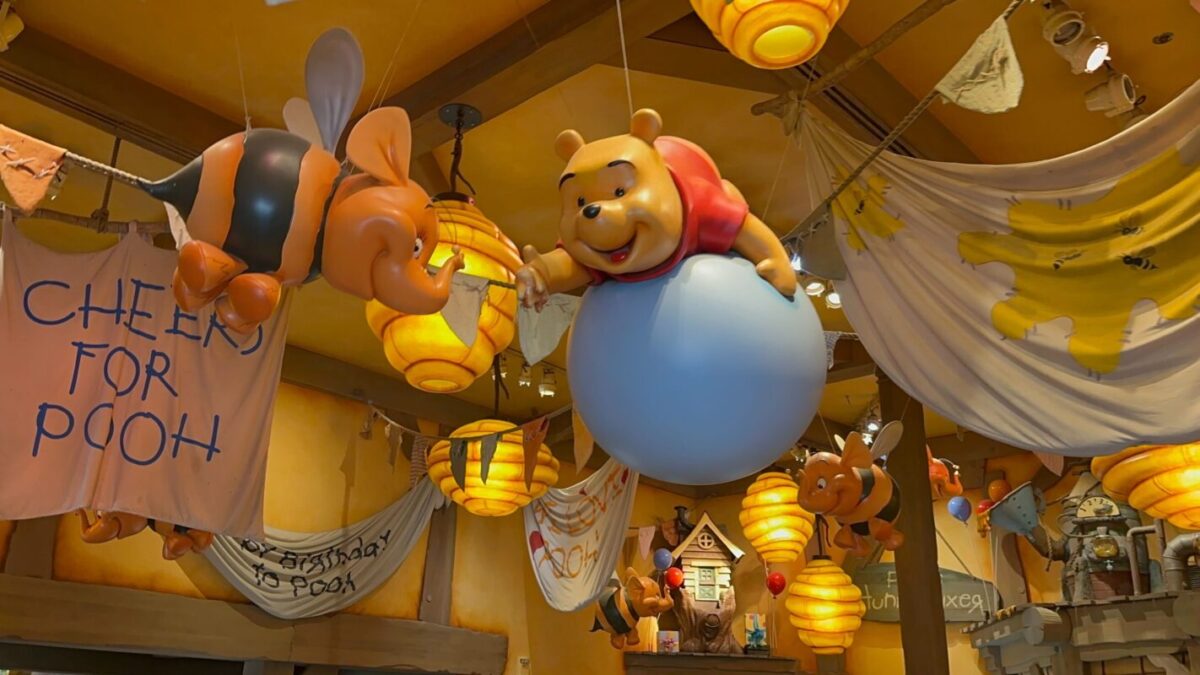 Decorative ceiling display featuring winnie the pooh and friends hovering with balloons over a themed store, with "cheers for pooh" sign.