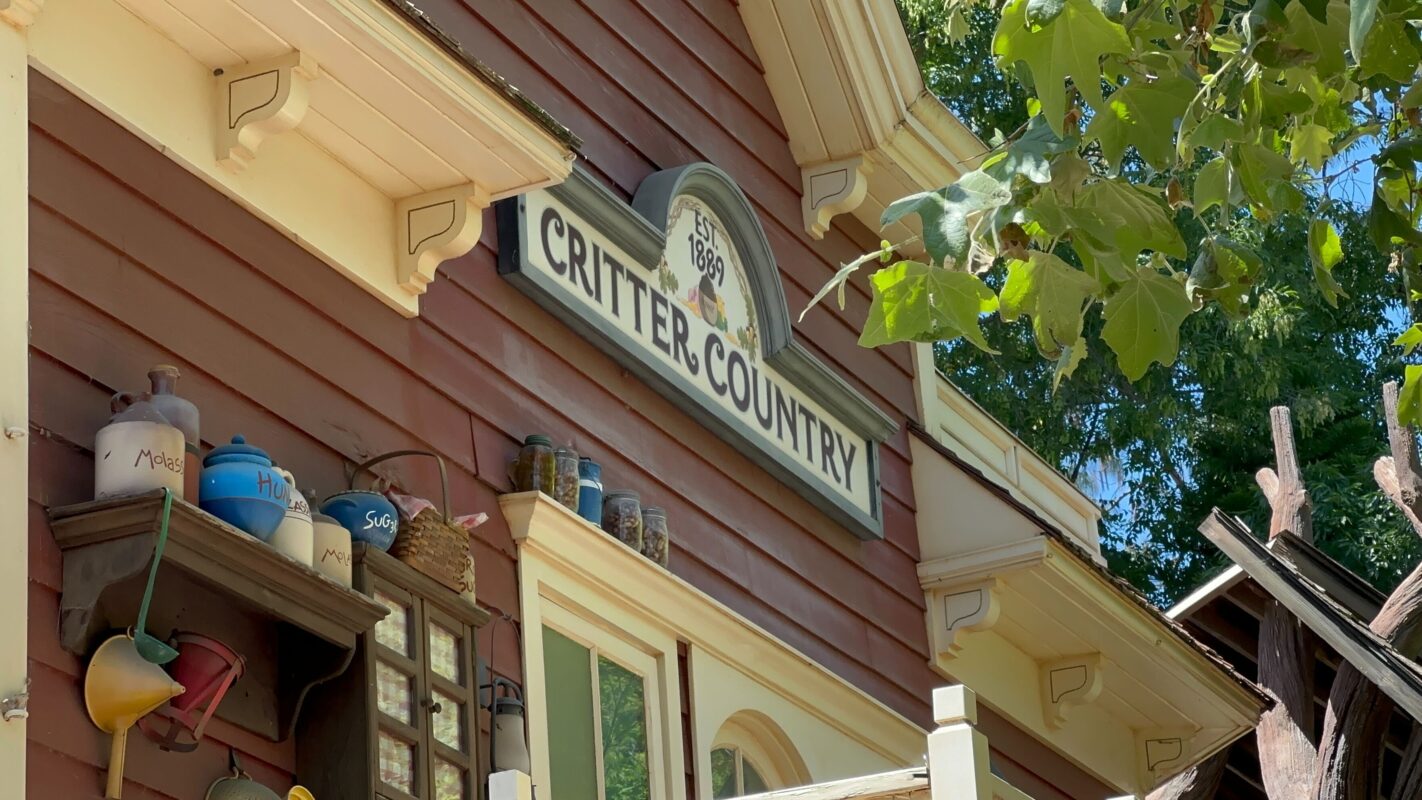 Sign reading "critter country" on a rustic wooden building adorned with various pots and artifacts under bright sunlight.