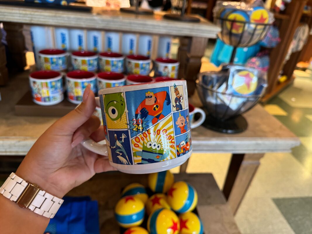 A reporter's hand holding a ceramic Pixar Fest mug.