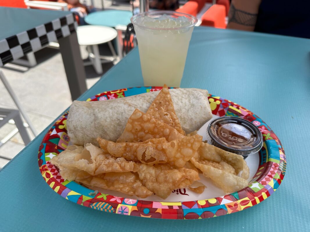 A plate with a burrito, crispy wontons, and a side of salsa, accompanied by a lime drink on a blue table.
