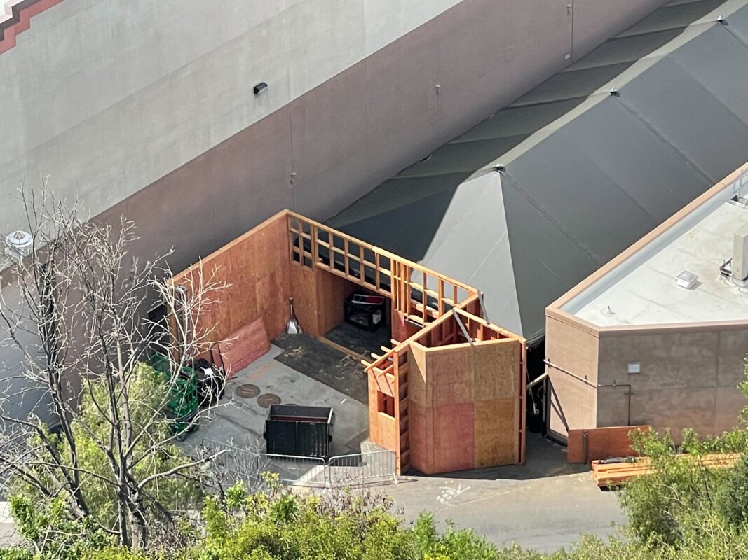 Aerial view of a small construction site with wooden framing and scattered building materials near large gray buildings prepared for Halloween Horror Nights 2024.