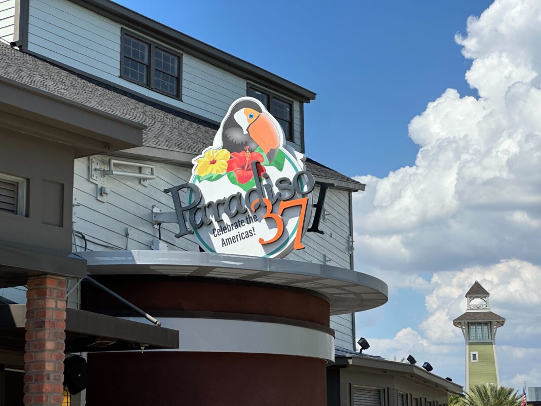 A vibrant sign for "paradiso 37" featuring a toucan with a beach-themed design on a building, under a blue sky with clouds.
