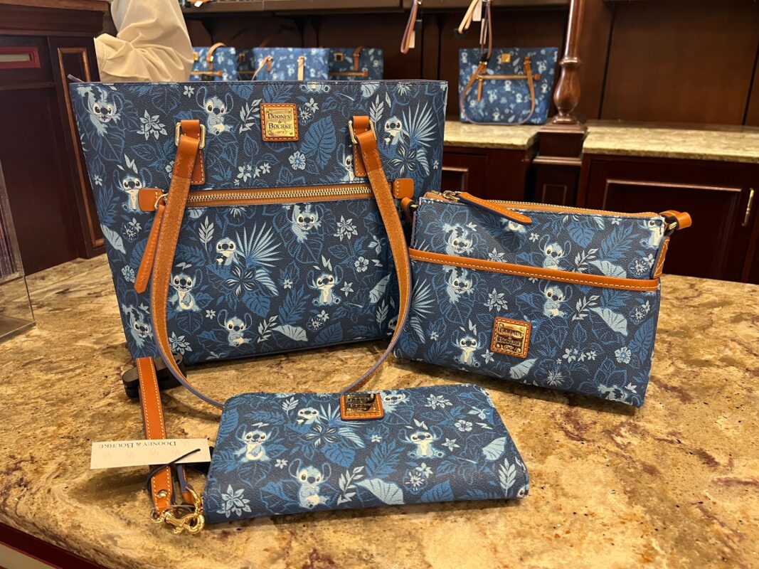 A collection of blue floral pattern handbags and wallets displayed on a marble countertop. The items feature tan leather accents and metal brand tags.