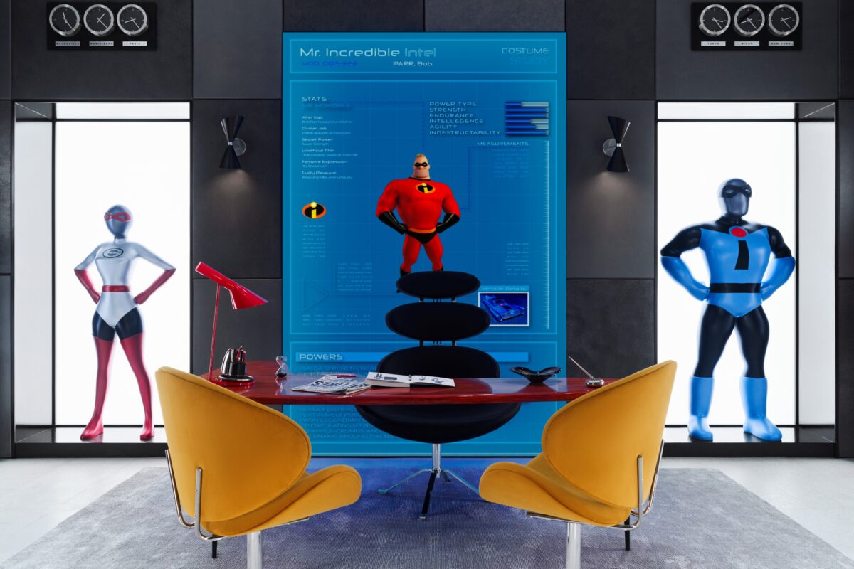 A modern office with a desk and two yellow chairs in front, featuring statues of superheroes in costumes and a large 'Mr. Incredible Intel' display on the wall behind.