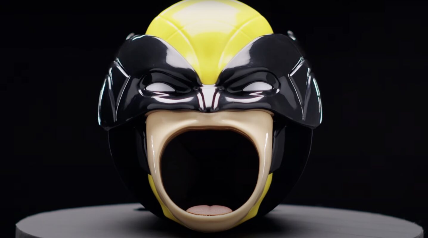 A ceramic mug resembling a helmet or mask with a black, yellow, and white color scheme, featuring an open mouth design—perfect for any Wolverine fan.