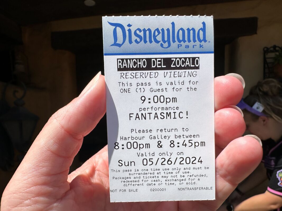 A hand holding a Disneyland park ticket for reserved viewing of Fantasmic on May 26, 2024, at 9:00 PM. The ticket is valid for one guest and needs to be redeemed at Harbour Galley by 8:45 PM.