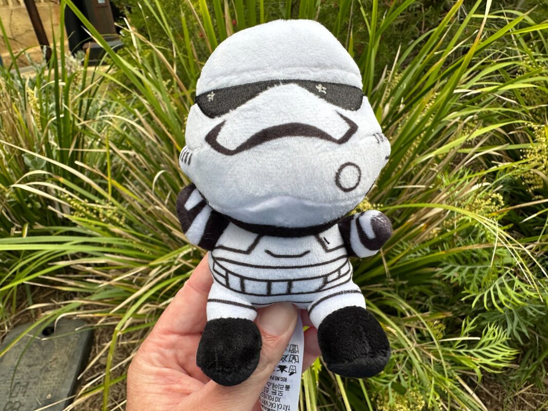 A Wishables plush toy resembling a stormtrooper from Star Wars, positioned against a backdrop of green plants.