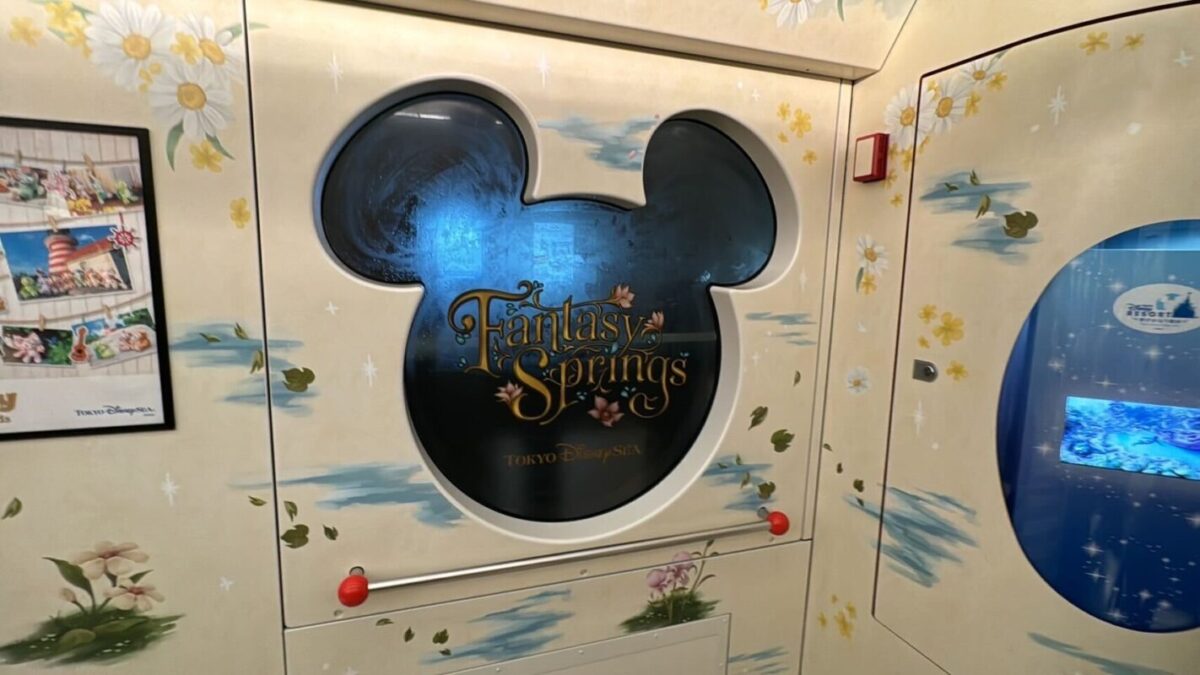 Decorative wall with a mickey mouse-shaped emblem for "fantasy springs" at tokyo disneysea, surrounded by floral patterns and an aquarium window on the right.