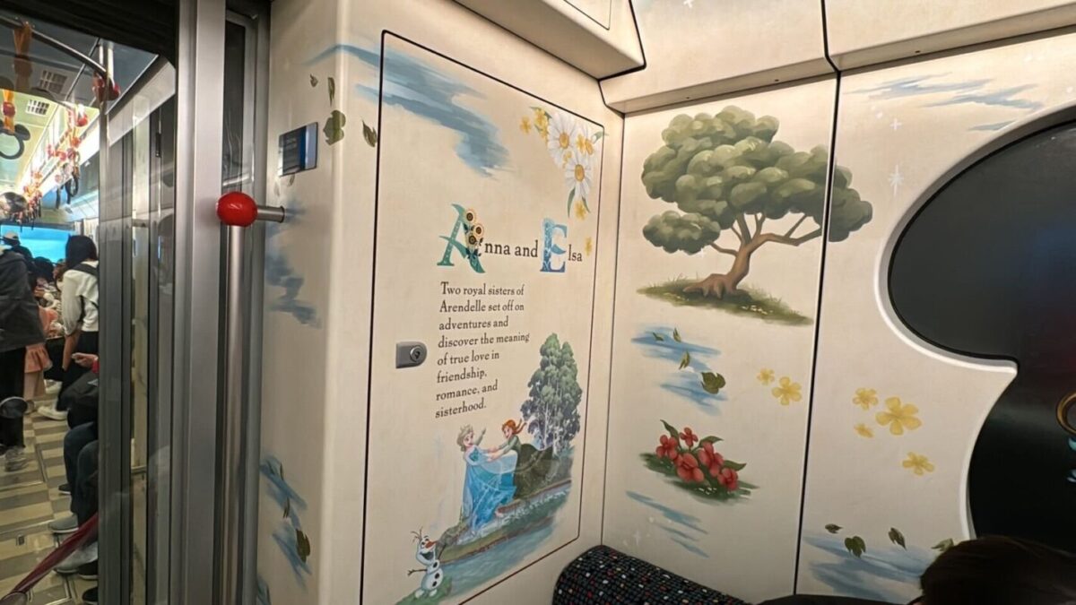 Interior of a train car with whimsical illustrations on the walls, depicting a story about a tree and a leaf, visible through the open train door.