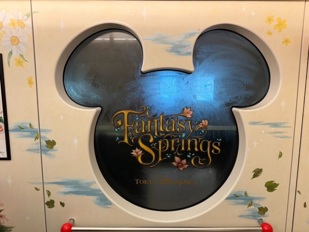 Decorative panel at tokyo disneysea featuring the iconic mickey mouse silhouette and the logo for fantasy springs, adorned with painted floral accents.