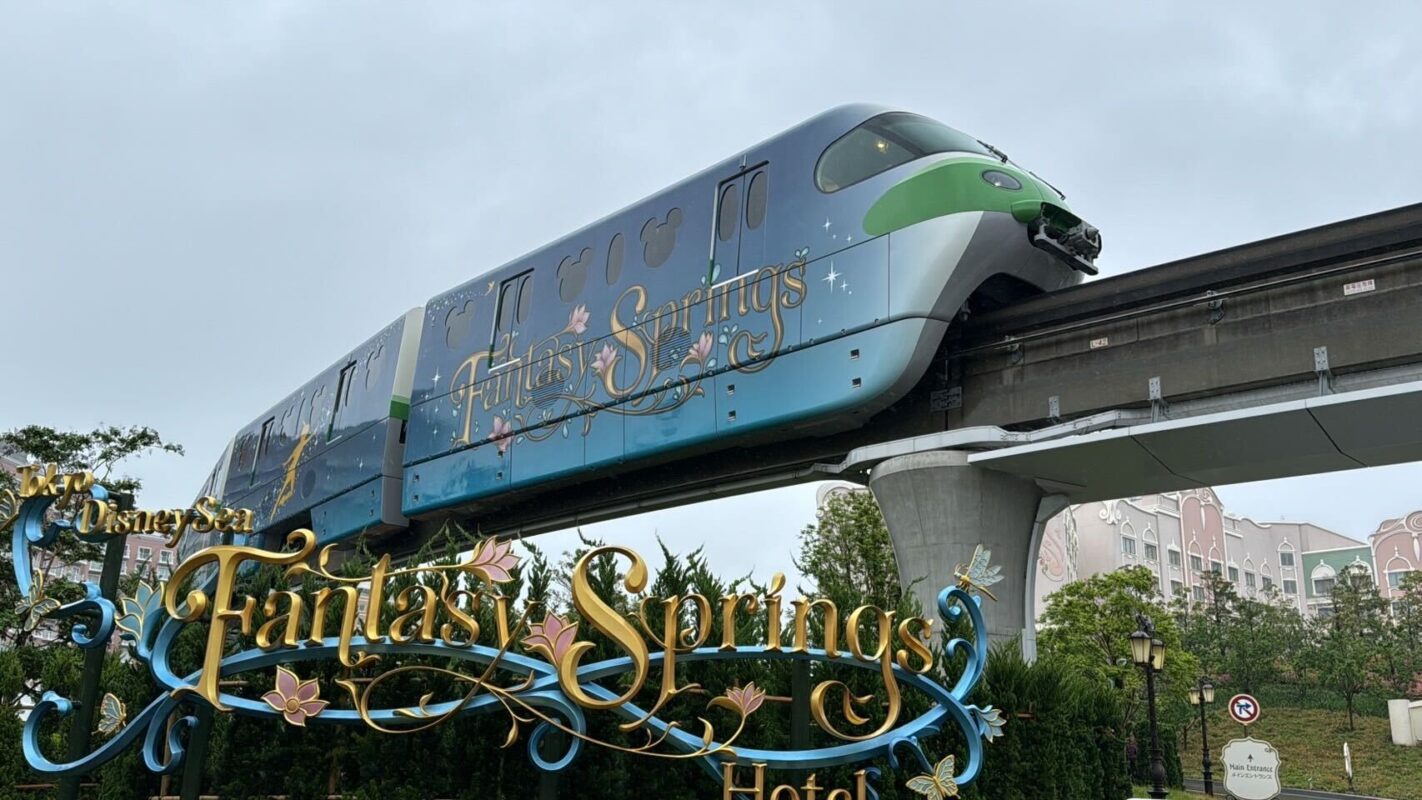 Decorative Monorail with "Tokyo DisneySea Fantasy Springs" wrap on elevated track against a cloudy sky above Fantasy Springs Hotel sign.