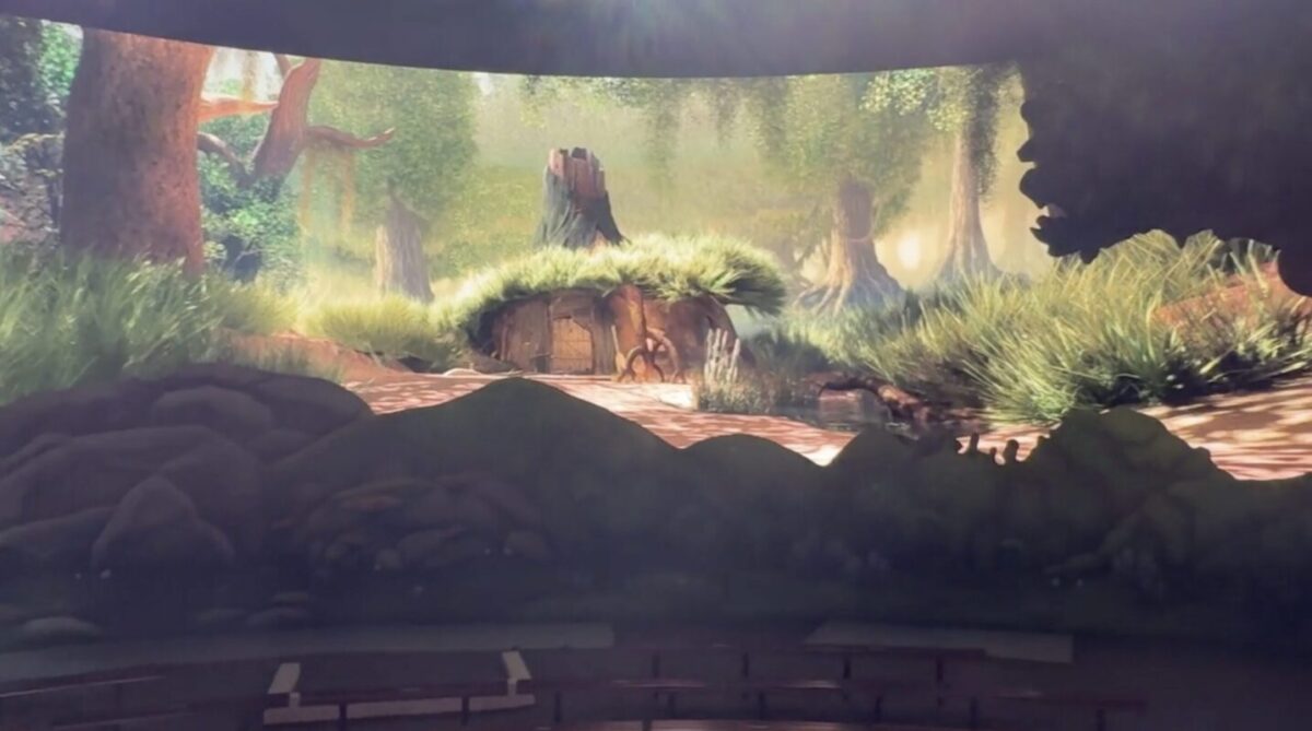 A vibrant woodland scene with a small house built into a hill, surrounded by tall trees and lush greenery. Soft sunlight filters through the trees, casting shadows on the ground.