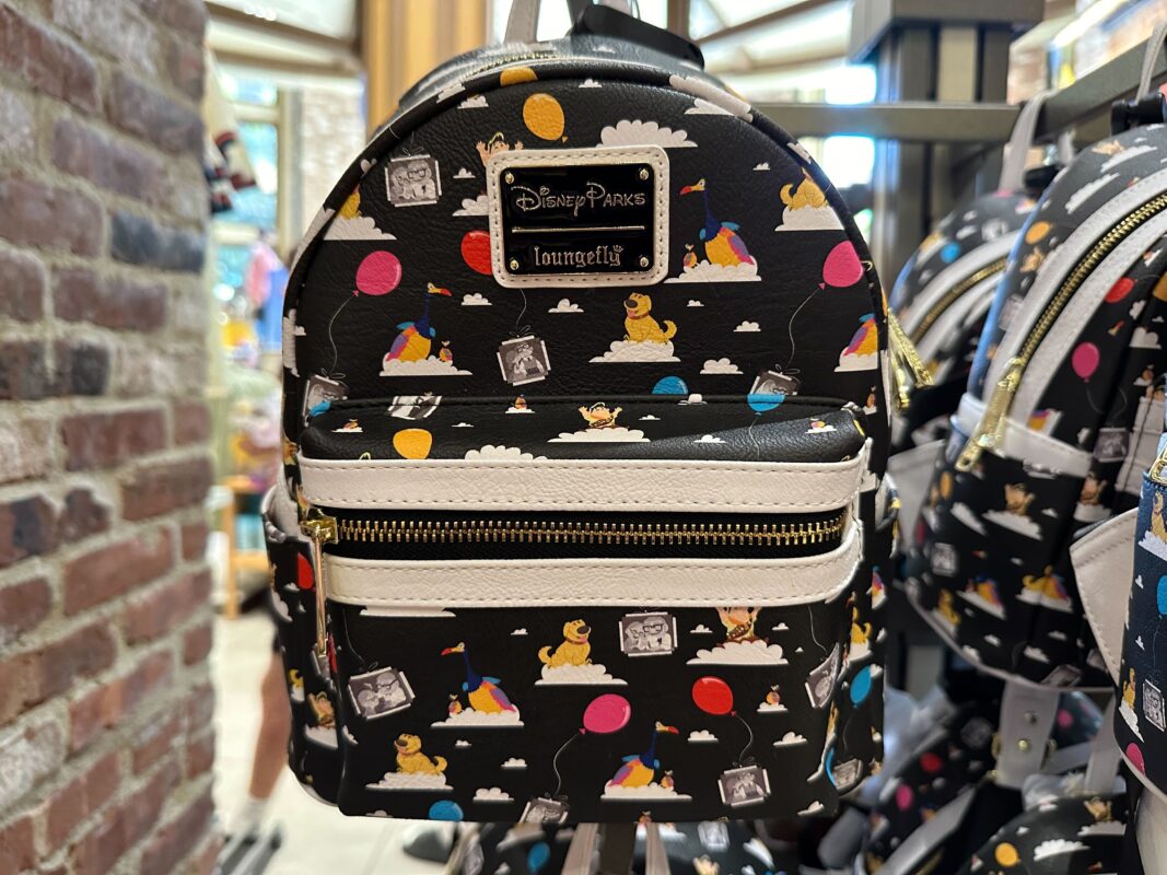 Close-up of a black Disney Parks 'Up' Loungefly Backpack featuring colorful graphics of characters and balloons, displayed on a store rack.