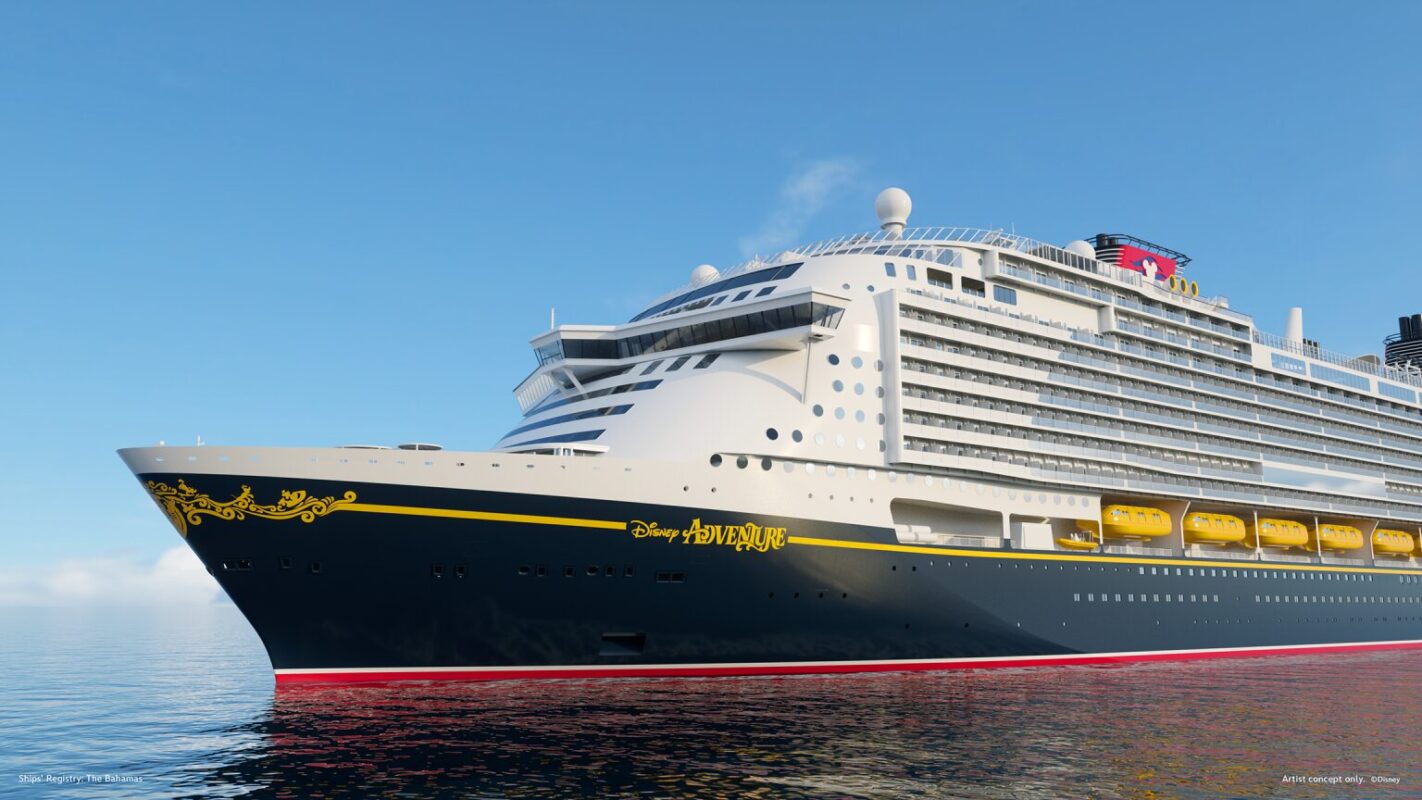 A large white cruise ship with black and yellow accents named "Disney Adventure" is sailing on calm blue water under a clear sky.