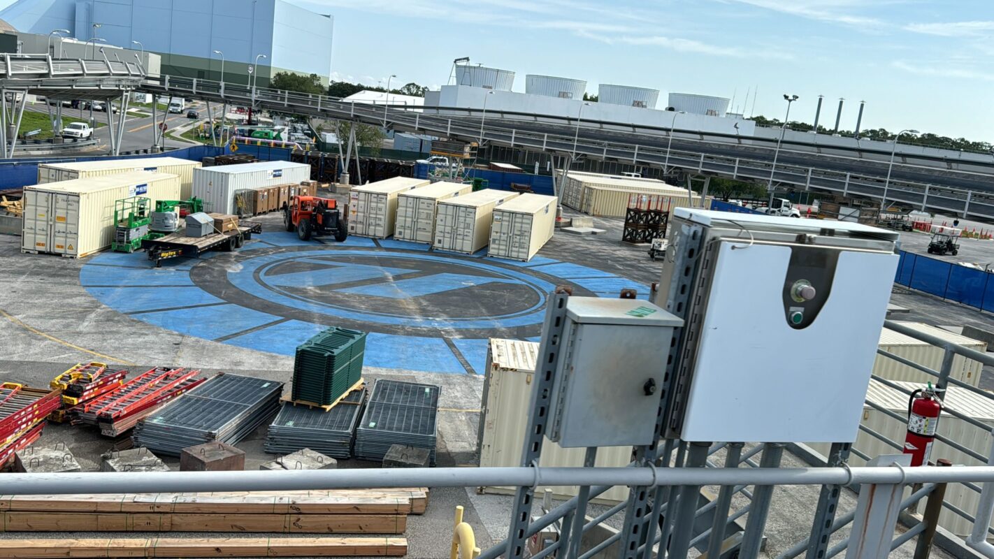 An industrial construction site with containers, building materials, and construction equipment. There is a circular blue marking on the ground, indicating a specific area for operations and test track activities.